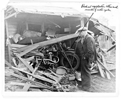 August 1940: a man looks at a motor bike damaged by falling timbers in a garden. A note on the photograph requests that the registration letters and numbers are blocked out