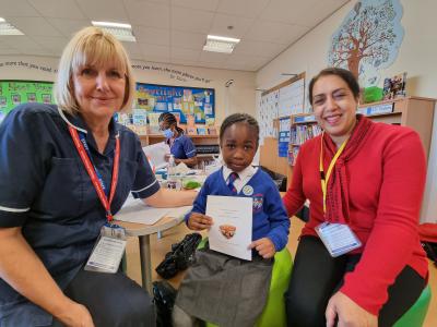 A Year 1 pupil at Rakegate Primary School is given her vaccination by Helen Burrell, Immunisation Nurse at Vaccination UK, watched by Councillor Jasbir Jaspal, Cabinet Member for Public Health and Wellbeing